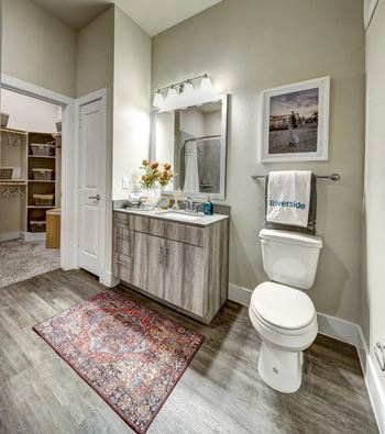 A bathroom with a rug on the floor and a toilet next to a sink.